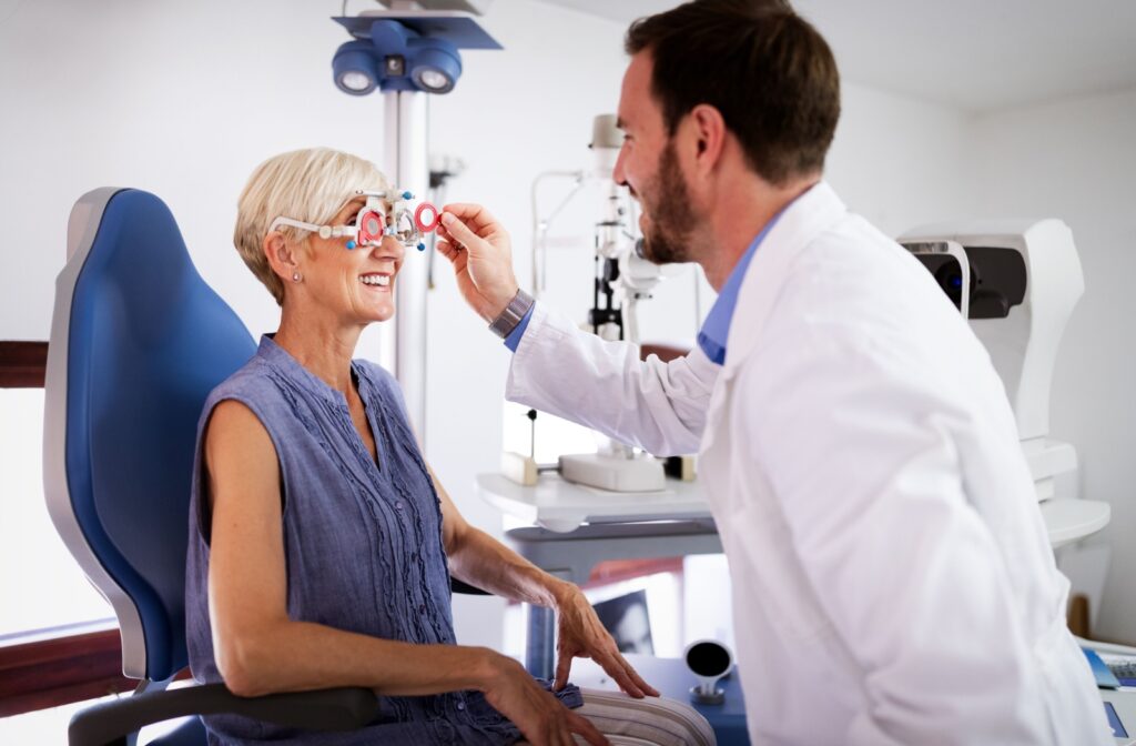 young male optometrist placing trial frames on smiling mature female patient.