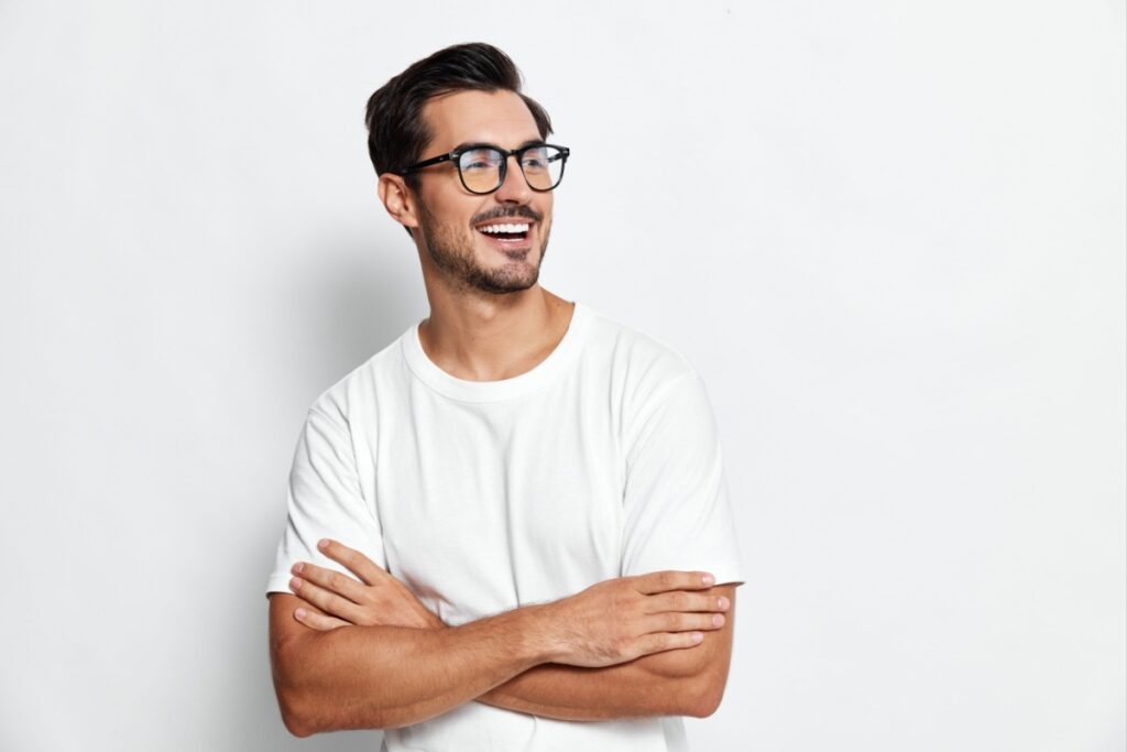 Young happy man standing against a wall wearing dark frames